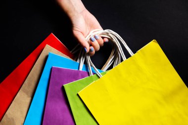 Siyah bir arka planda renkli kağıt torbalarla el ele tutuşmak. Ekolojik kavram.