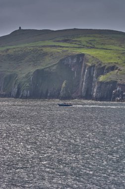 İrlanda, Dingle 'da büyük bir uçurumun önünde tekne sürüyor. Dingle, İrlanda 'da yunus mantarı arayan turist teknesi.