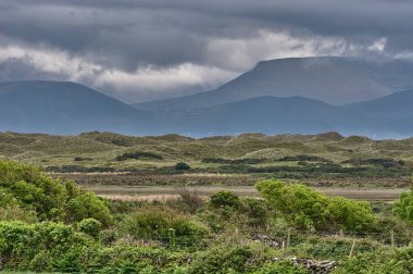 İrlanda, Dingle Yarımadası 'ndaki güzel panoramik manzara. Arkasında dağ siluetleri ve koyu yağmur bulutları olan panoramik kumul manzarası. Inch Sahili, İrlanda 'da fırtınalı hava.