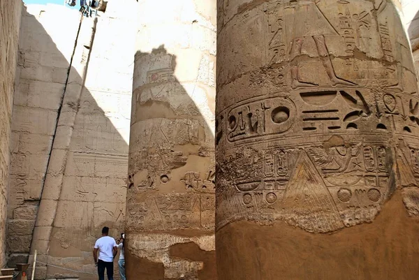 観光客はカルナック寺院の巨大な石の柱に刻まれた古代エジプトの象形文字を読もうとします。エジプトの豪邸。ユネスコ世界遺産. — ストック写真
