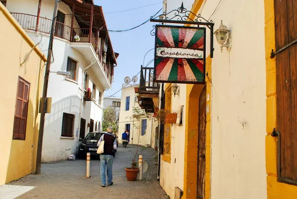Girne, Kyrenia, Kuzey Kıbrıs. Mayıs 2019. Aktif yetişkin erkek turist güneşli bir günde dar bir sokakta kafelerle yürüyor.. 