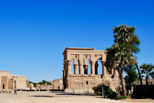 I turisti visitano Trajans Kiosk accanto al padiglione del Tempio Philae con palme in primo piano. È sull'isola di Agilkia nel fiume Nilo. Patrimonio Mondiale UNESCO. Assuan Egitto — Foto Stock