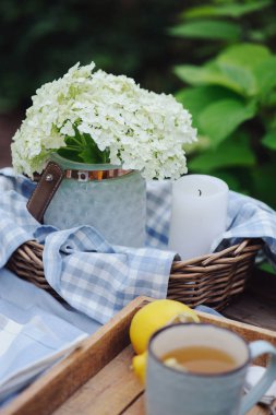 Summer breakfast in beautiful blooming garden. Tea with lemon, hydrangea flowers on wooden table with green background. Summertime and country slow living concept clipart