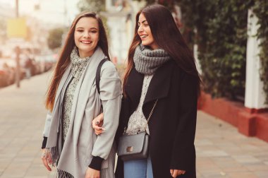 iki genç mutlu kız rahat moda kıyafetler içinde şehrin sokaklarında yürürken, sıcak palto giyen ve having fun