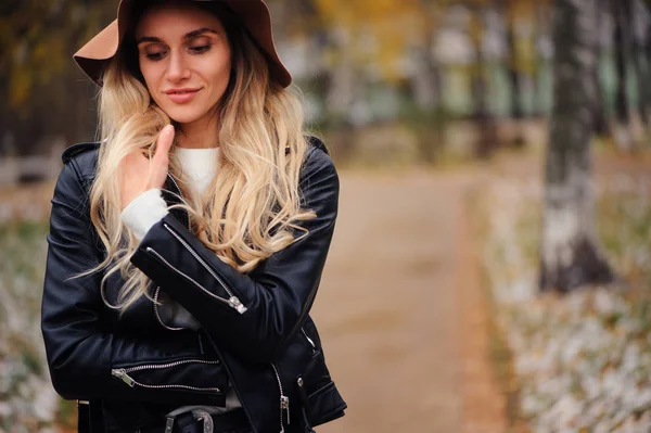 屋外を歩く若い幸せな女性の肖像画を秋ファッション秋帽子と革のジャケットの公園 — ストック写真