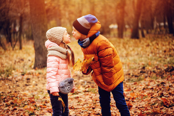 Осенний портрет счастливых детей, играющих на открытом воздухе в парке. Улыбающиеся брат и сестра ходят в солнечный день в теплых вязаных шляпах и шарфах
