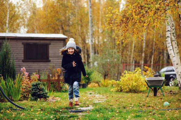 happy kid girl running in late autumn garden with wooden shed on background