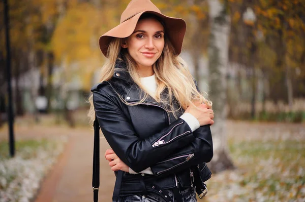 屋外を歩く若い幸せな女性の肖像画を秋ファッション秋帽子と革のジャケットの公園 — ストック写真