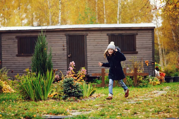 happy kid girl running in late autumn garden with wooden shed on background