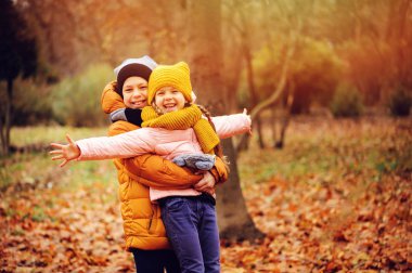 Park'ta açık oynayan mutlu çocuklar sonbahar portresi. Güneşli bir günde yürüyüş kardeş gülümseyen, giyen sıcak şapka ve bere örgü