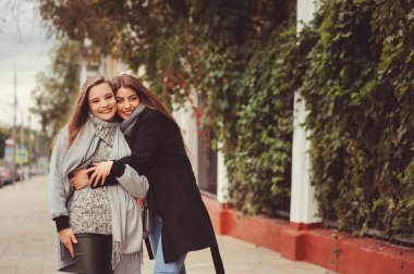 iki genç mutlu kız rahat moda kıyafetler içinde şehrin sokaklarında yürürken, sıcak palto giyen ve having fun