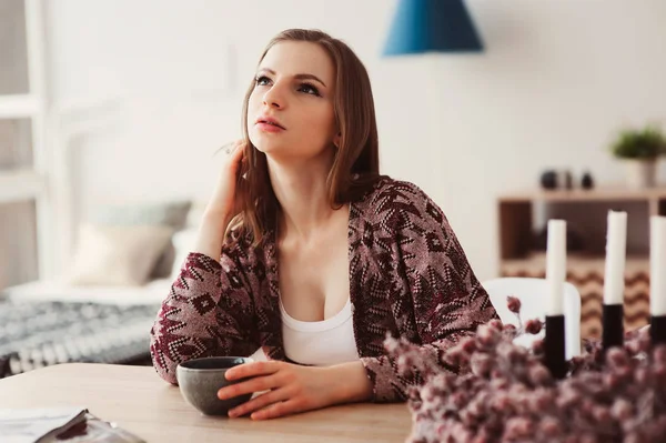 young beautiful woman relaxing at home in the morning, having breakfast in modern loft kitchen with scandinavian interior