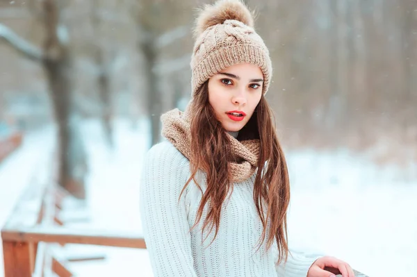 winter close up portrait of beautiful young woman in knitted hat and sweater walking in snowy park or forest, spending weekend outdoo