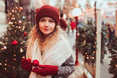 Noel Şehir sokakta yürüyen mutlu genç kadın dekore çelenk, oyuncaklar ve ağaçlar, tatil alışveriş kavramı ile