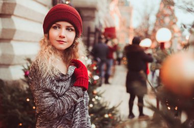 Noel Şehir sokakta yürüyen mutlu genç kadın dekore çelenk, oyuncaklar ve ağaçlar, tatil alışveriş kavramı ile