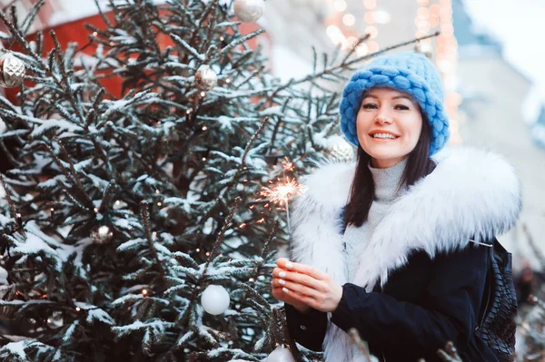 クリスマス幸せと女性のポートレート燃焼かこう歩いて屋外白い毛皮と特大チャンク ファッション コート雪の冬市にニット帽子 — ストック写真