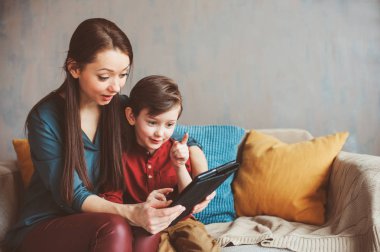mutlu anne ve yürümeye başlayan çocuk oğlu kullanarak evde tablet. Aile bilgisayar oynarken ya da internet, elektronik cihazlar ve modern yaşamın çocuklarda arama