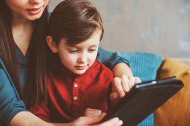 mutlu anne ve yürümeye başlayan çocuk oğlu kullanarak evde tablet. Aile bilgisayar oynarken ya da internet, elektronik cihazlar ve modern yaşamın çocuklarda arama