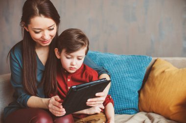 mutlu anne ve yürümeye başlayan çocuk oğlu kullanarak evde tablet. Aile bilgisayar oynarken ya da internet, elektronik cihazlar ve modern yaşamın çocuklarda arama