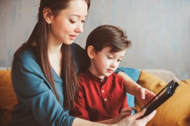 mutlu anne ve yürümeye başlayan çocuk oğlu kullanarak evde tablet. Aile bilgisayar oynarken ya da internet, elektronik cihazlar ve modern yaşamın çocuklarda arama
