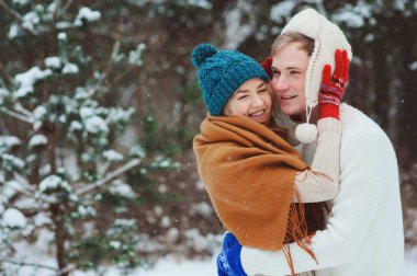 mutlu genç sevgi dolu çift karlı kış ormanda yürüyüş eğlenceli ve sarılmak sahip kar ile kaplı. Etkin kış tatil açık.