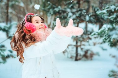 Pembe kulaklıklı mutlu kızın kış portresi. Karlı kış ormanlarında dışarıda yürüyor. Mutlu çocukluklar ve aktif kış tatili konsepti