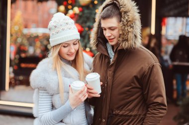 mutlu çift sıcak mulled şarap veya şehir sokaklarında yürüyüş çay ile Noel portresi için tatil, Noel ağacı ışıkları ve arka plan üstünde toys ile dekore edilmiş