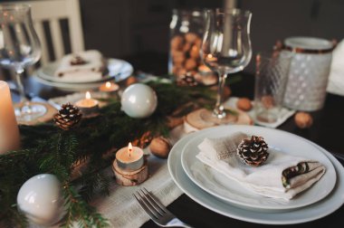 Şenlikli Noel ve Yeni Yıl sofrası İskandinav tarzında hazırlandı. Kırsal ve beyaz tonlarda el yapımı detaylarla. Çam kozalakları, dallar ve mumlarla süslenmiş yemek salonu.