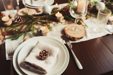 Şenlikli Noel ve Yeni Yıl sofrası İskandinav tarzında hazırlandı. Kırsal ve beyaz tonlarda el yapımı detaylarla. Çam kozalakları, dallar ve mumlarla süslenmiş yemek salonu.