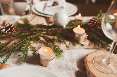 Şenlikli Noel ve Yeni Yıl sofrası İskandinav tarzında hazırlandı. Kırsal ve beyaz tonlarda el yapımı detaylarla. Çam kozalakları, dallar ve mumlarla süslenmiş yemek salonu.
