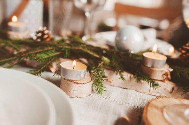 Şenlikli Noel ve Yeni Yıl sofrası İskandinav tarzında hazırlandı. Kırsal ve beyaz tonlarda el yapımı detaylarla. Çam kozalakları, dallar ve mumlarla süslenmiş yemek salonu.