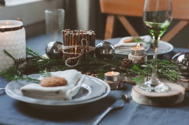 Şenlikli Noel ve Yeni Yıl sofrası İskandinav tarzında hazırlandı. Kırsal ve beyaz tonlarda el yapımı detaylarla. Çam kozalakları, dallar ve mumlarla süslenmiş yemek salonu.
