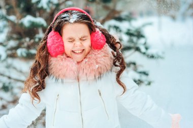 Pembe kulaklıklı mutlu kızın kış portresi. Karlı kış ormanlarında dışarıda yürüyor. Mutlu çocukluklar ve aktif kış tatili konsepti