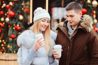 mutlu çift sıcak mulled şarap veya şehir sokaklarında yürüyüş çay ile Noel portresi için tatil, Noel ağacı ışıkları ve arka plan üstünde toys ile dekore edilmiş
