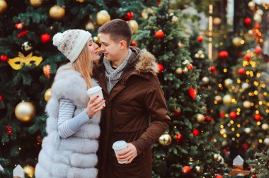 mutlu çift sıcak mulled şarap veya şehir sokaklarında yürüyüş çay ile Noel portresi için tatil, Noel ağacı ışıkları ve arka plan üstünde toys ile dekore edilmiş