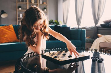 Akıllı çocuk kız oyun dama evde yaşam tarzı vurdu. Masa oyunları için çocuklar kavramı, modern iç gerçek insanlarla samimi serisi