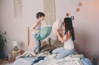mutlu anne ve çocuk evlat oyun yastık yatakta sabahın erken saatlerinde mücadele. Aile rahat yaşam tarzı serisi.