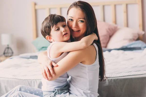 快乐的爱的母亲拥抱幼儿儿子在卧室在周末上午 — 图库照片