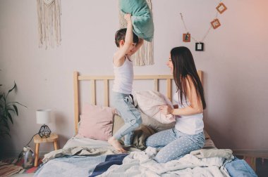 mutlu anne ve çocuk evlat oyun yastık yatakta sabahın erken saatlerinde mücadele. Aile rahat yaşam tarzı serisi.