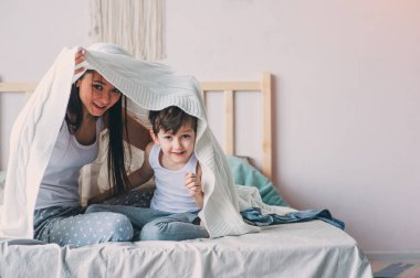 mutlu anne ve oğlu oynayan ve sıcak hafta sonu sabah yatakta battaniyenin altında saklanıyor. Gerçek aile ile rahat yaşam tarzı