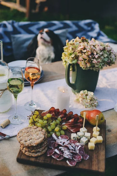 wine, cheese, ham and fruits served on wooden cutting board. Summer outdoor garden party