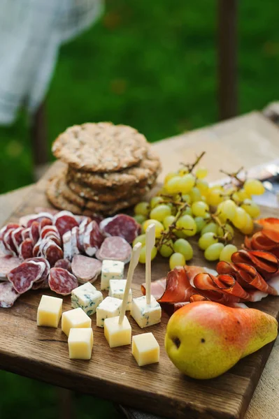 summer outdoor table with cheese and ham plate on cutting board with fruits and wine in glasses. Romantic dinner outdoor