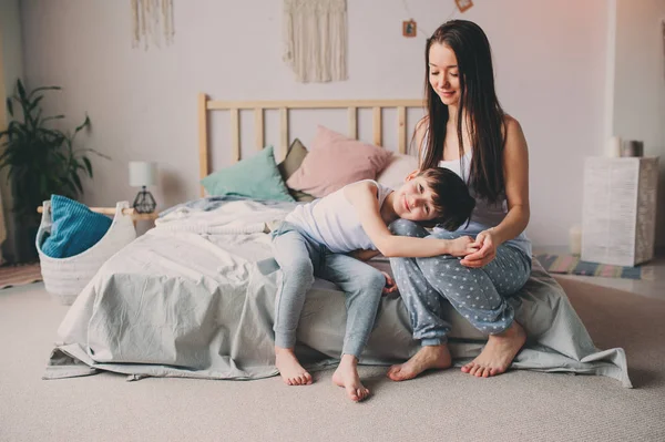 快乐的母亲早上抱着她的幼儿儿子 坐在家里的床上 休闲生活 家庭生活 — 图库照片