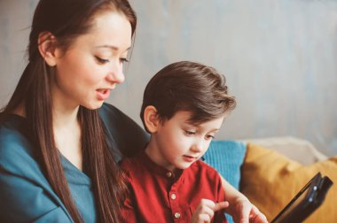 mutlu anne ve yürümeye başlayan çocuk oğlu kullanarak evde tablet. Aile bilgisayar oynarken ya da internet, elektronik cihazlar ve modern yaşamın çocuklarda arama