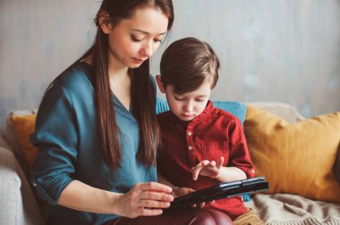 mutlu anne ve yürümeye başlayan çocuk oğlu kullanarak evde tablet. Aile bilgisayar oynarken ya da internet, elektronik cihazlar ve modern yaşamın çocuklarda arama