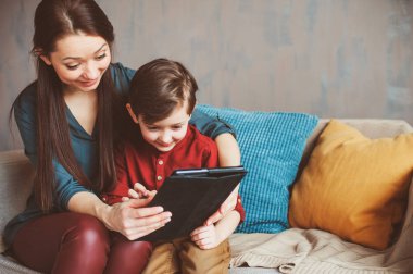 mutlu anne ve yürümeye başlayan çocuk oğlu kullanarak evde tablet. Aile bilgisayar oynarken ya da internet, elektronik cihazlar ve modern yaşamın çocuklarda arama