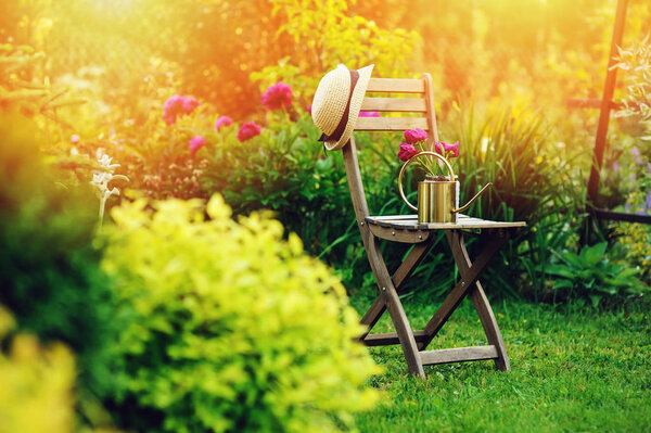beautiful blooming summer private garden with wooden chair, gardener hat and watering can