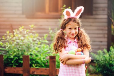Paskalya yumurtası avı açık ahşap kır evinde oynarken komik tavşan kulakları kız mutlu çocuk portresi