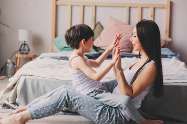 Yatak odasında çocuk oğlu ile oynarken annesi. Mutlu aile sabah pijama giymiş