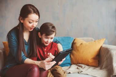 mutlu anne ve yürümeye başlayan çocuk oğlu kullanarak evde tablet. Aile bilgisayar oynarken ya da internet, elektronik cihazlar ve modern yaşamın çocuklarda arama